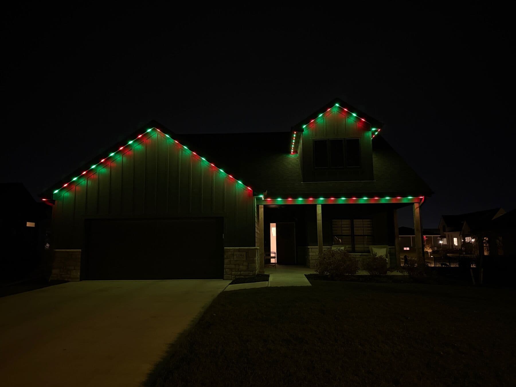 Red and green points along the gables and porch of a dark board-and-batten Omaha home