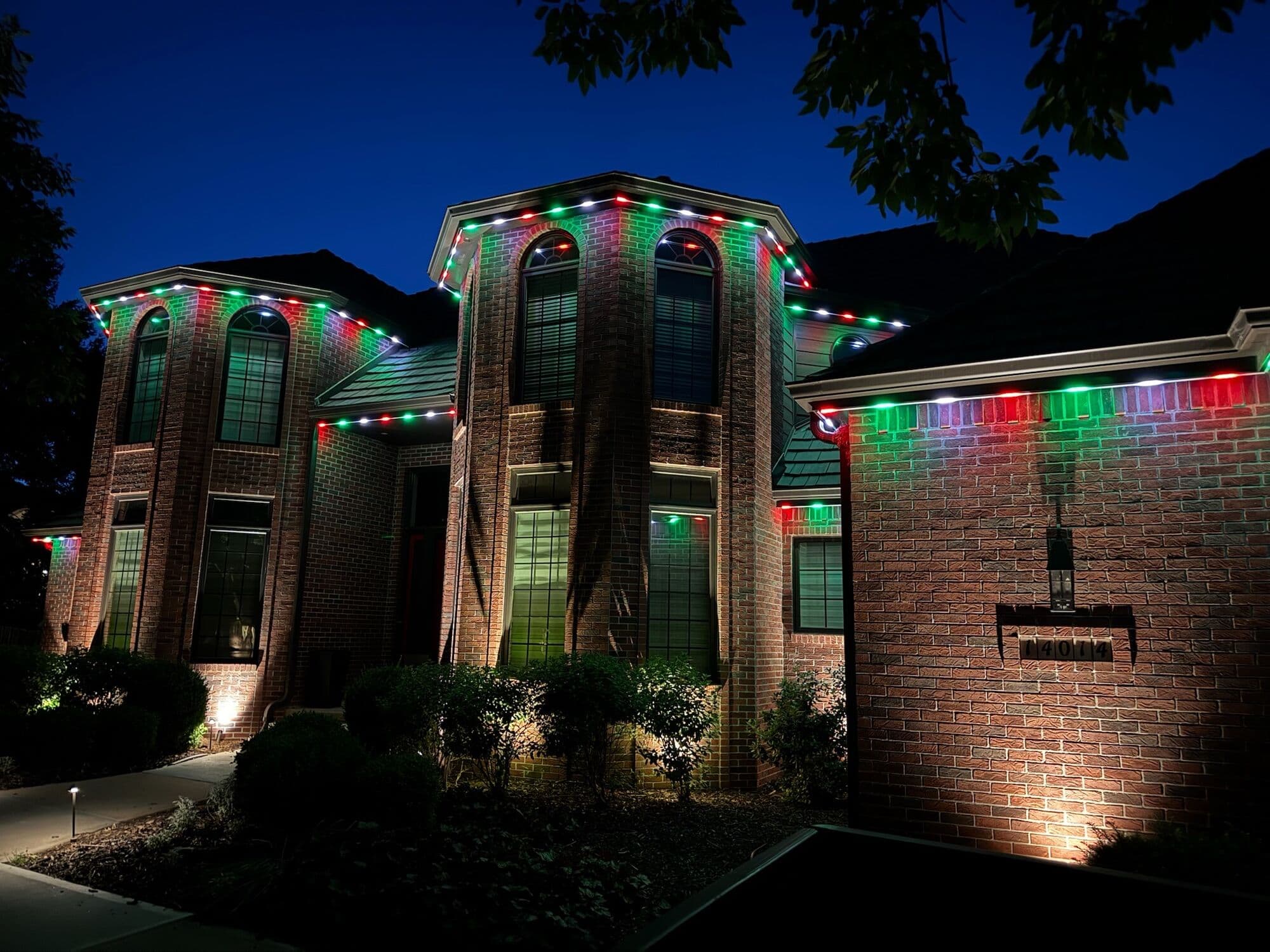 A large brick Omaha two-story in alternating red and green with uplights on the planting beds