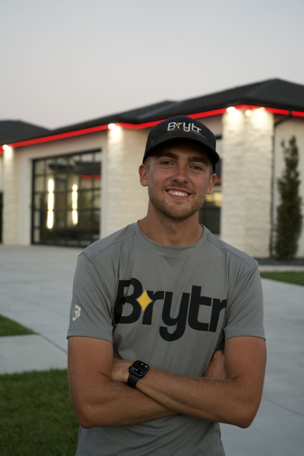 A Brytr installer in a Brytr shirt and cap outside a lit commercial building, its roofline run set to red