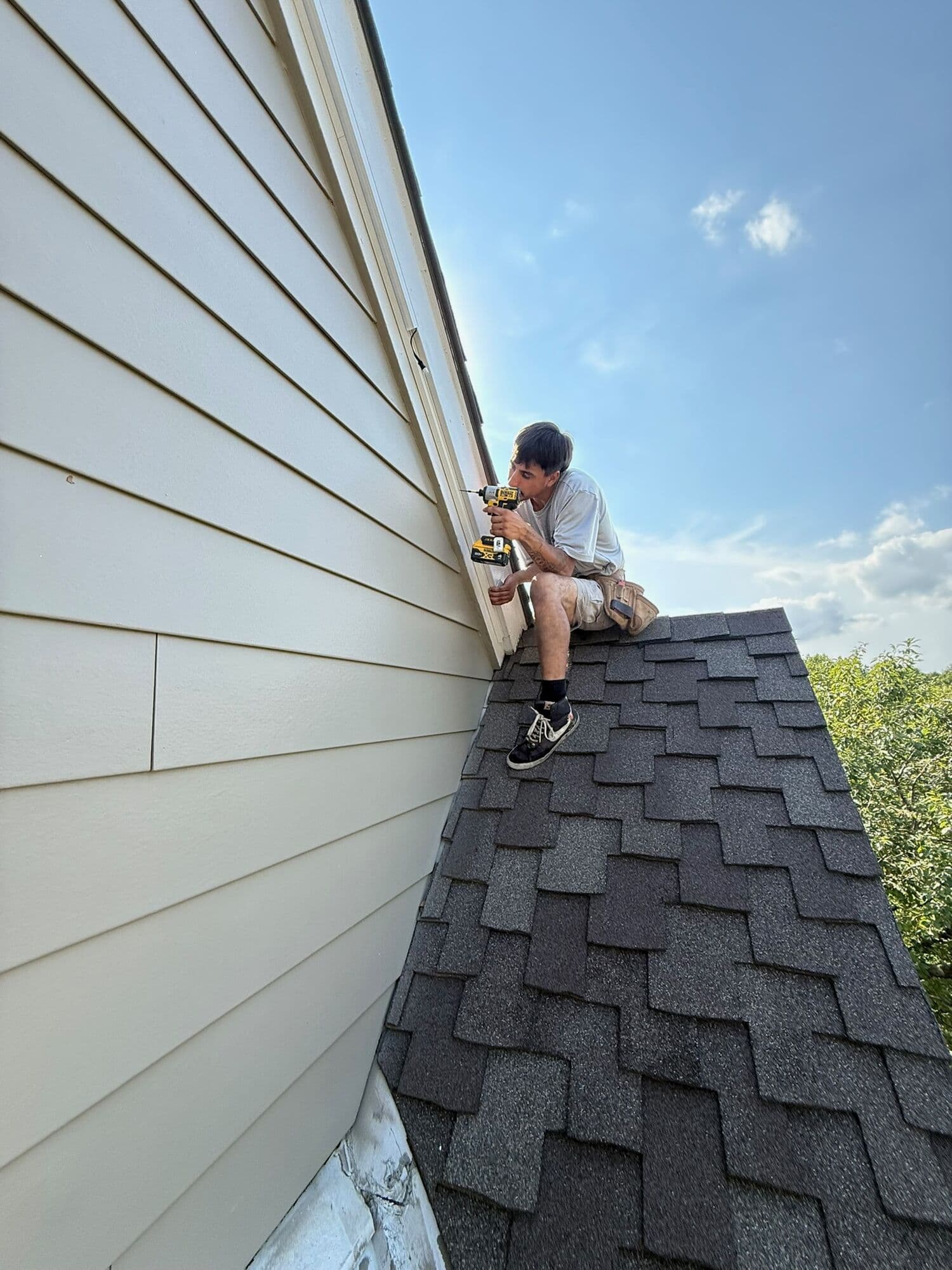 A Brytr installer sitting on the shingles of an Omaha roof in daylight, working along the line where the fascia meets the wall