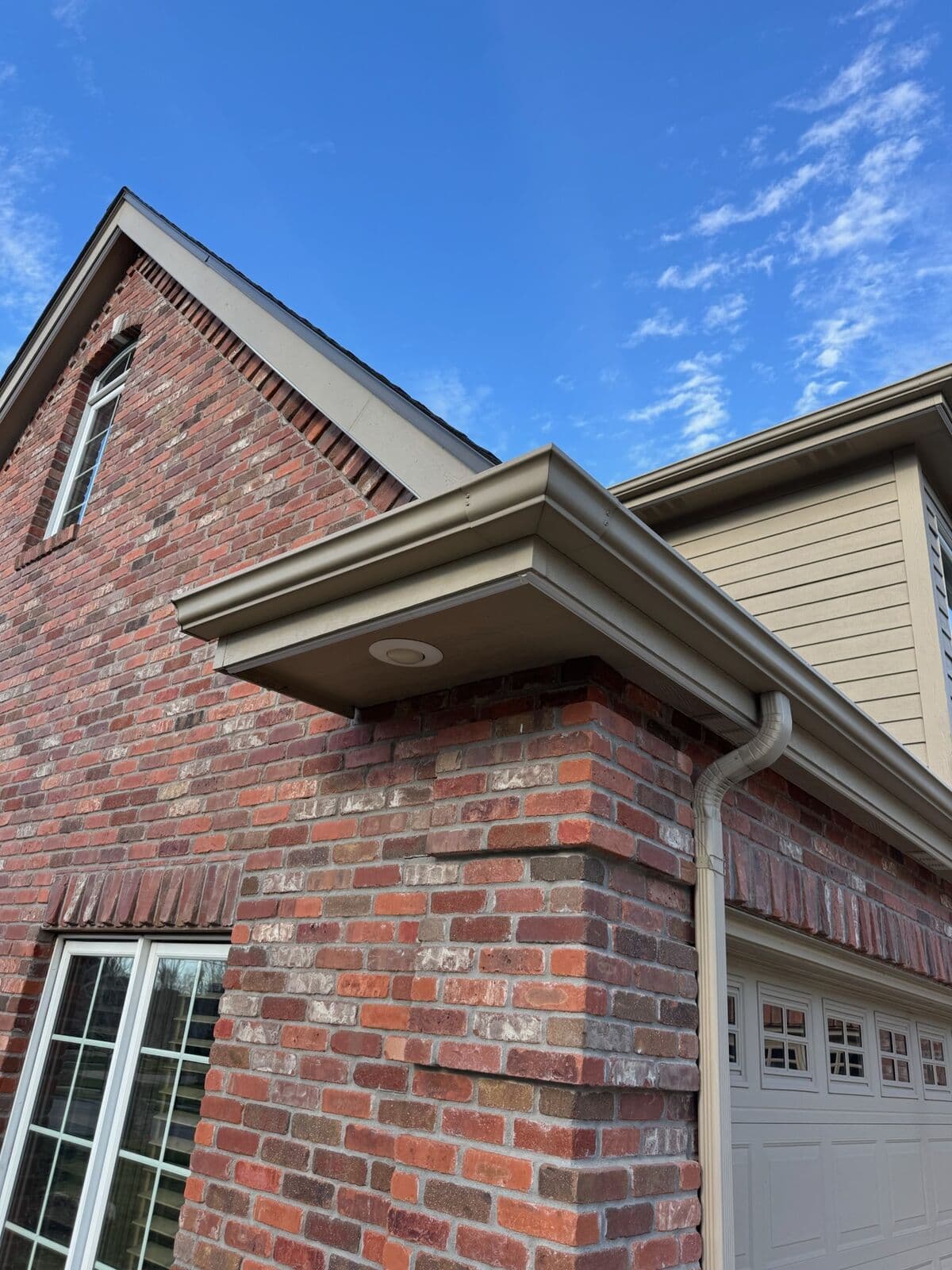A brick gable and white fascia on an Omaha home in daylight, the channel tucked under the roof edge as a slim line below the gutter
