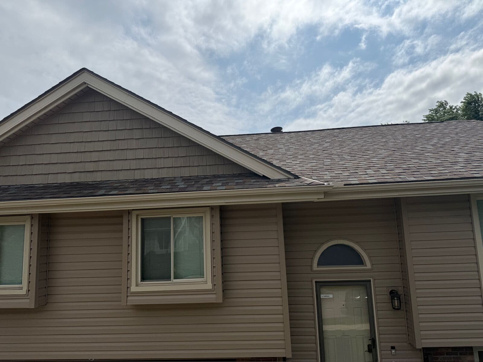 A shake gable meeting a shingled roof on an Omaha home in daylight, the run visible only as a narrow strip below the gutter line
