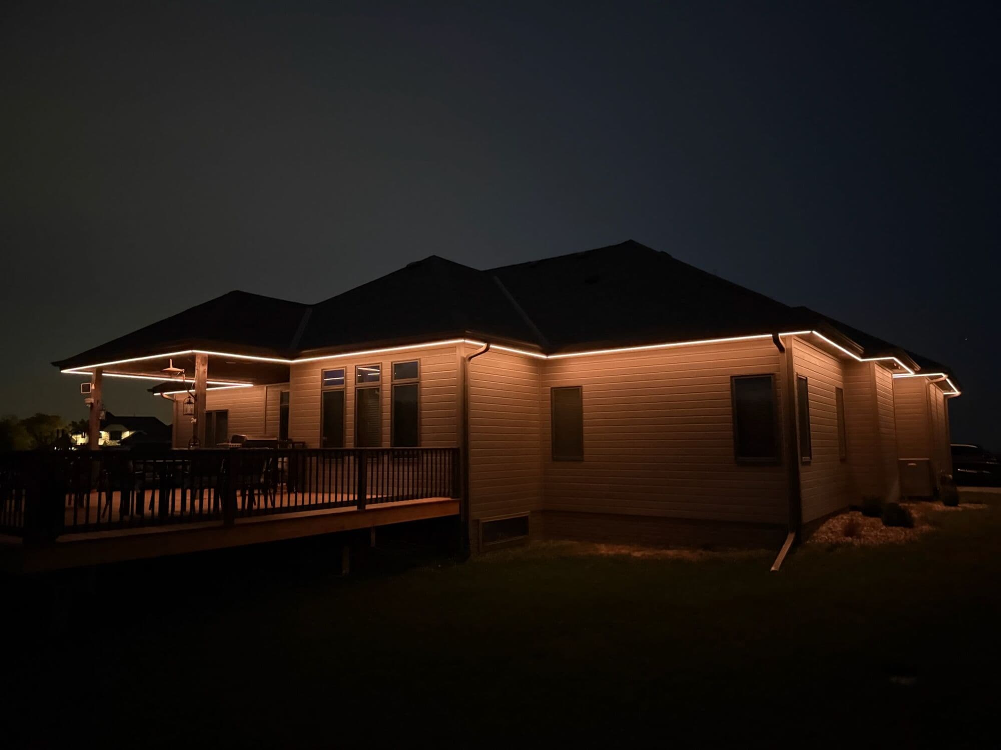 A long Omaha ranch at night with warm white along the roofline and a lit deck and pergola at one end