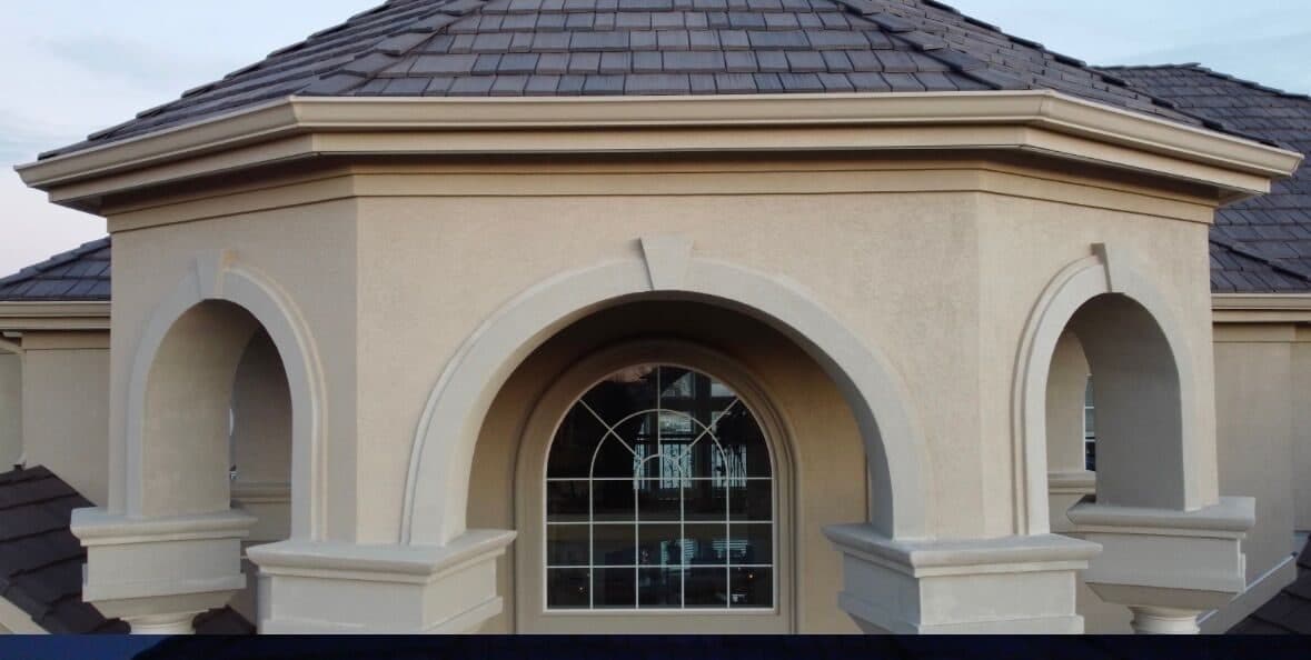 The stucco arched entry turret of an Omaha home in daylight, nothing visible under the roof edge