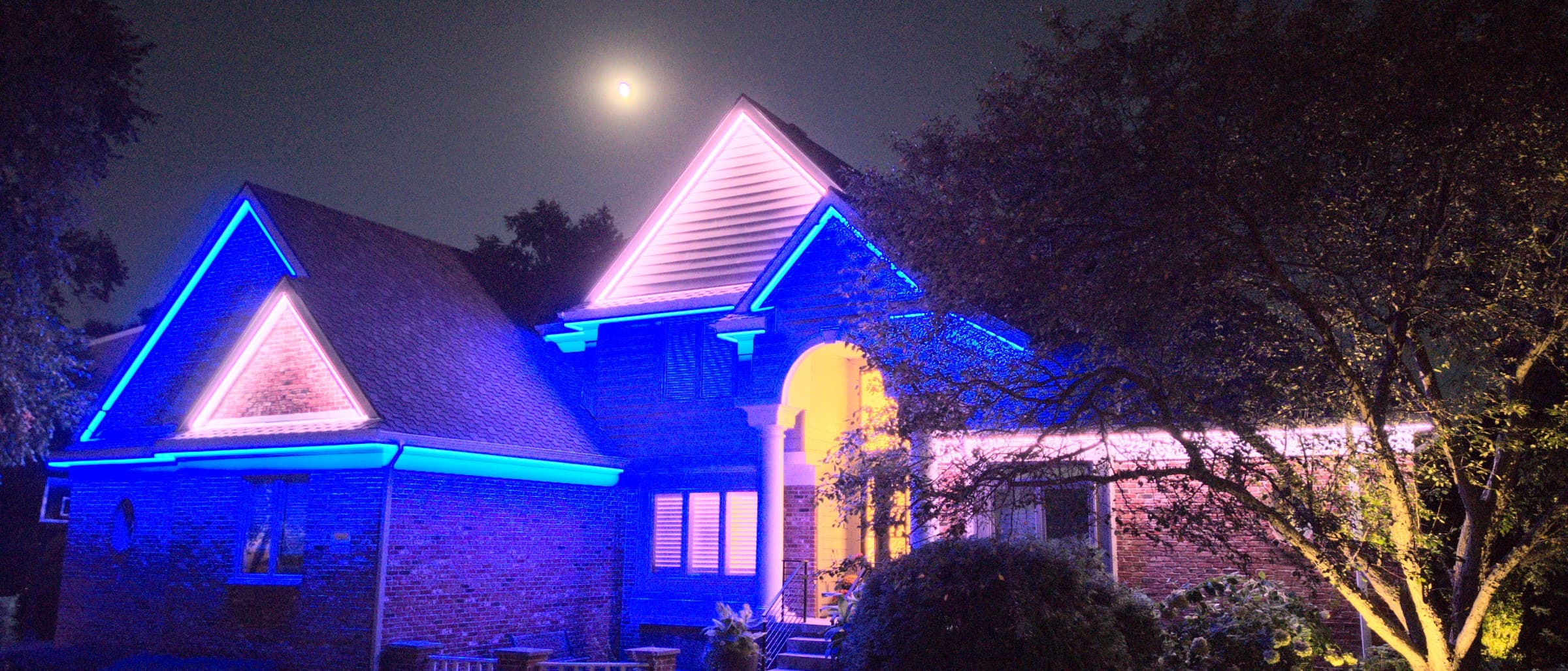 An Omaha home under a full moon with its roofline and gables lit, blue with the gables in warm white