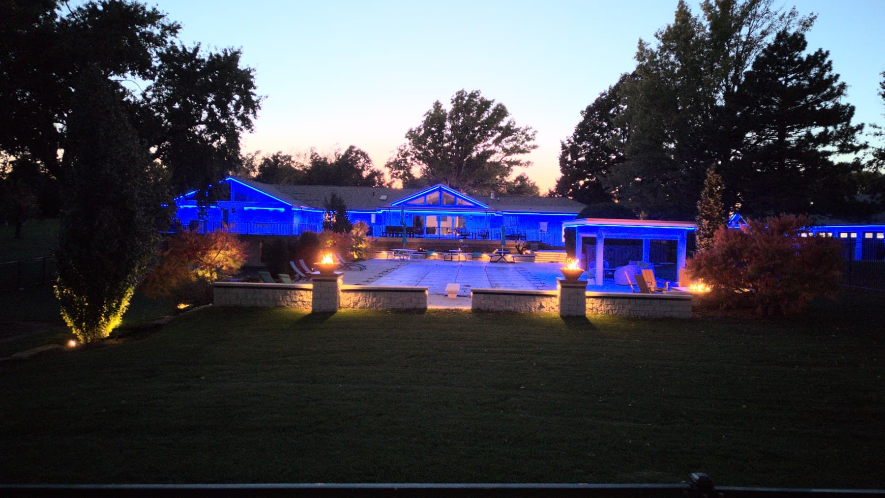 An Omaha home, pergola and pool deck lit blue at dusk