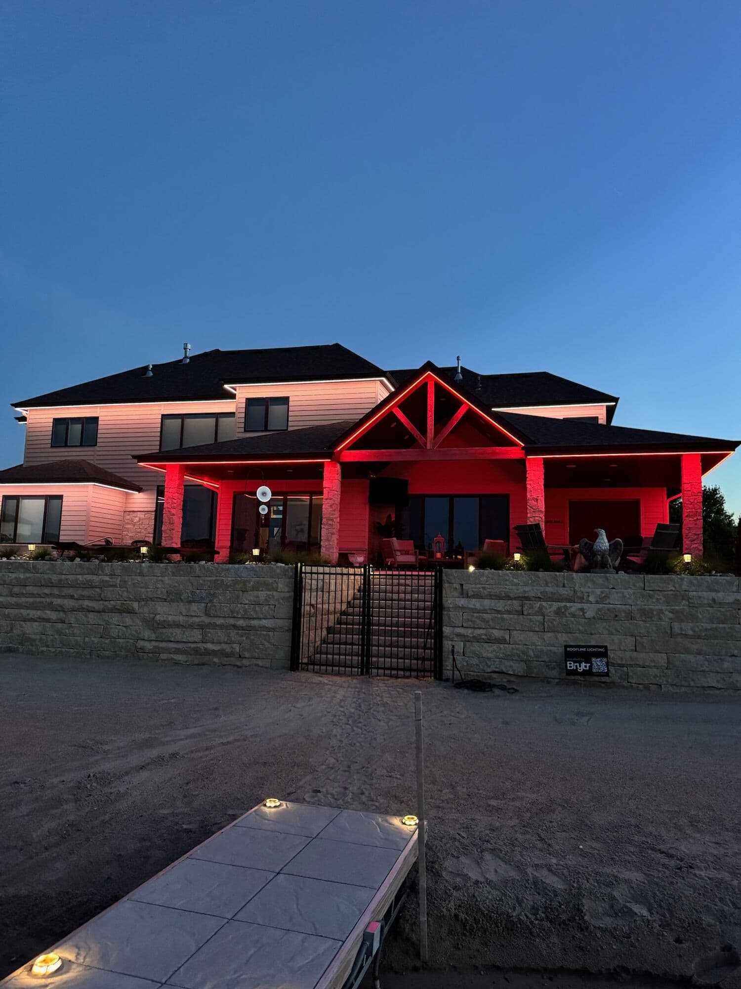 A stone seat wall with lit caps in the foreground and a covered porch behind it washed red at an Omaha home