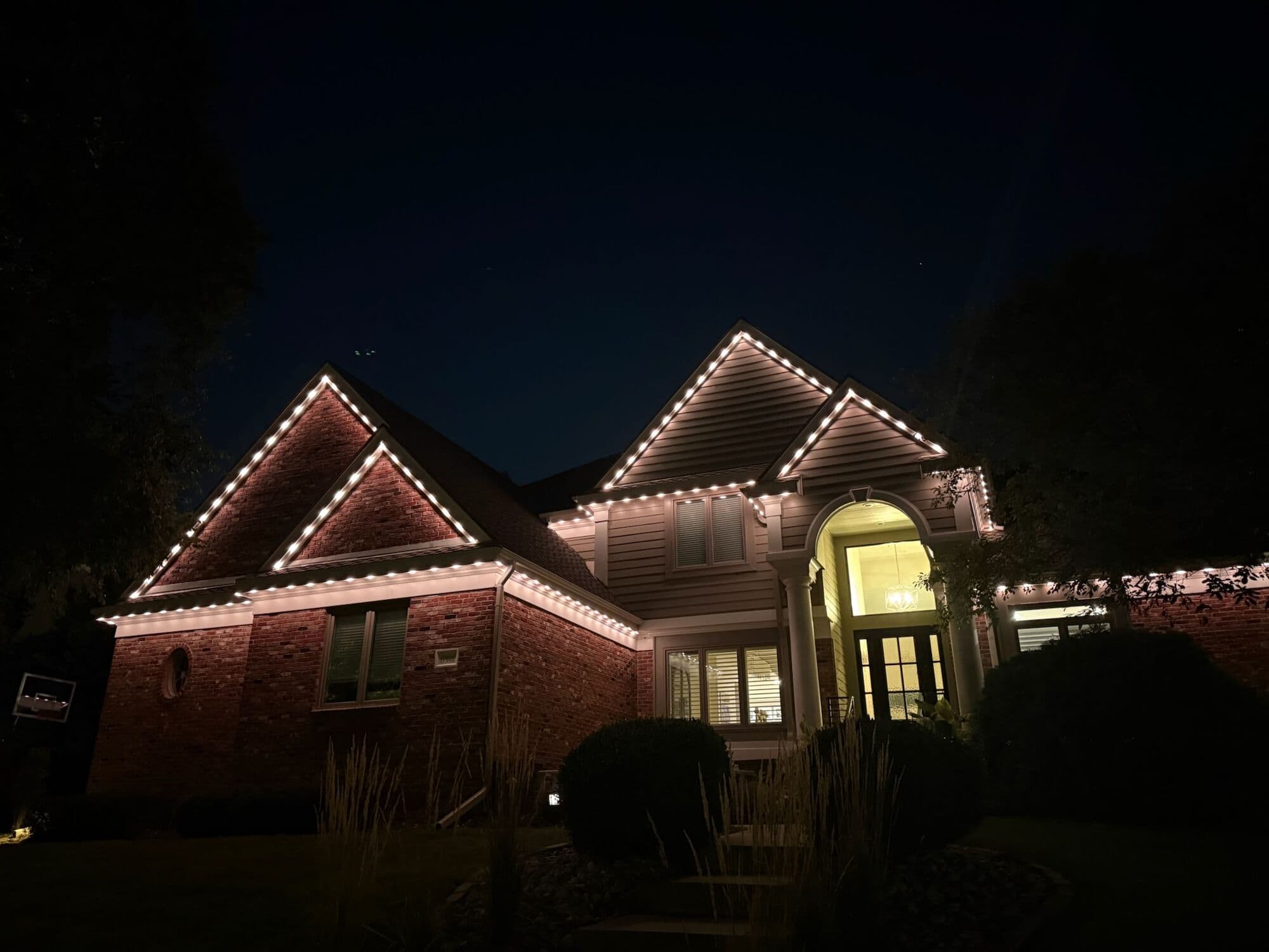 A brick Omaha home with several gables all lit warm, the entry glowing behind the glass