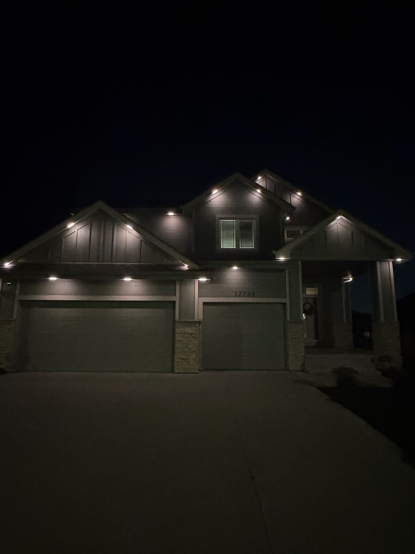 Warm white downlights spaced evenly under the eaves and gable peaks of a modern Omaha farmhouse