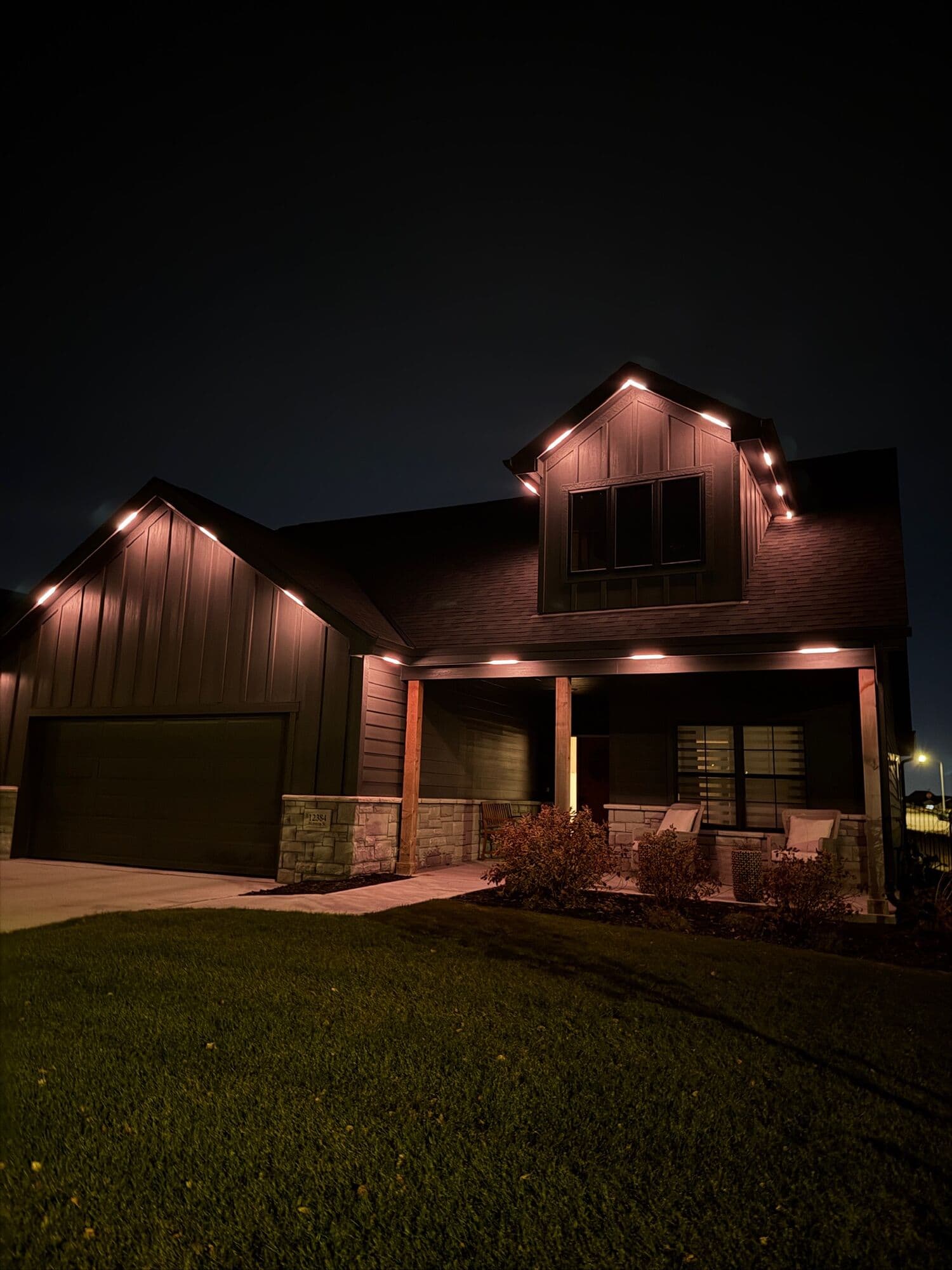 A dark-clad modern farmhouse in Omaha with a restrained warm white line along the roof edges