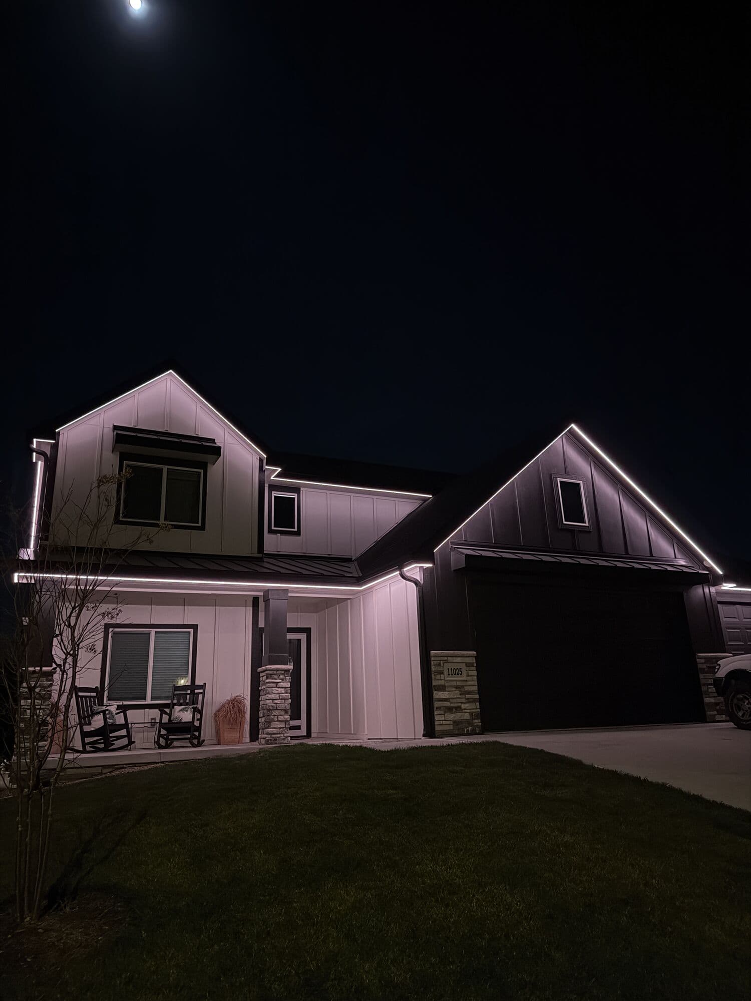 A white modern farmhouse in Omaha at night under a moon, its rooflines picked out in cool white