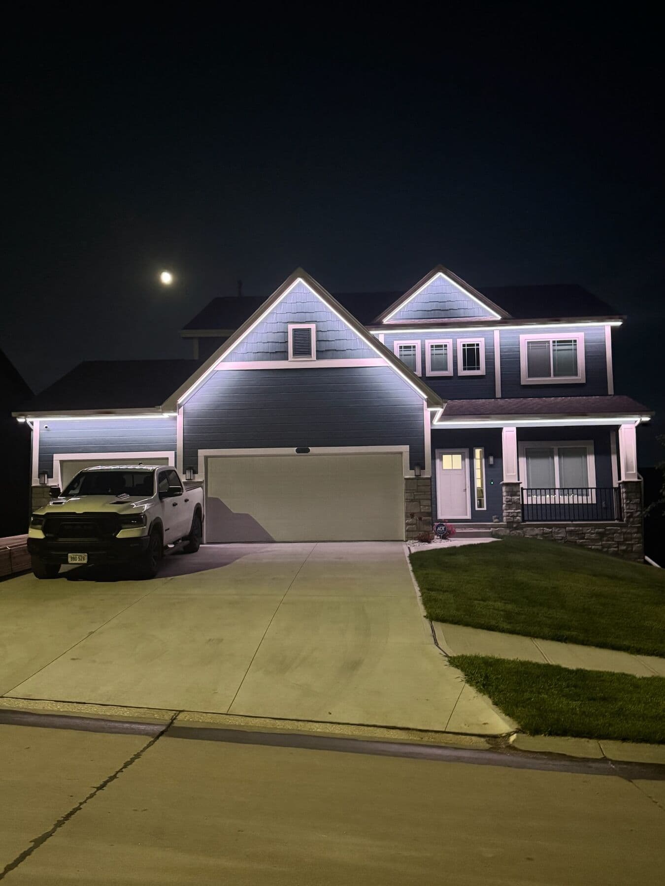 A gray Omaha two-story under a moon with cool white along the rooflines and a truck in the drive