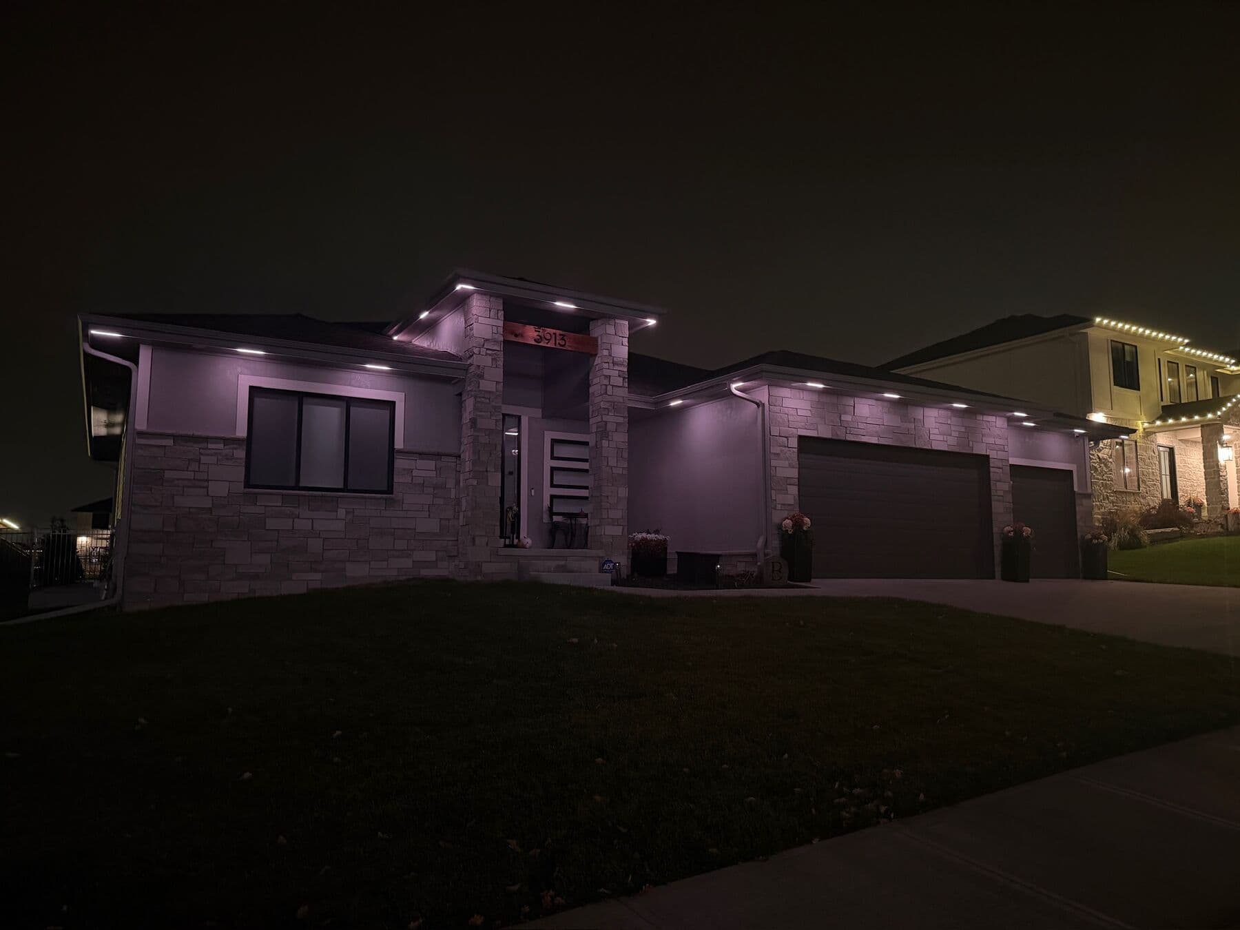 A modern stone and stucco Omaha two-story with warm downlights along the flat roof edges