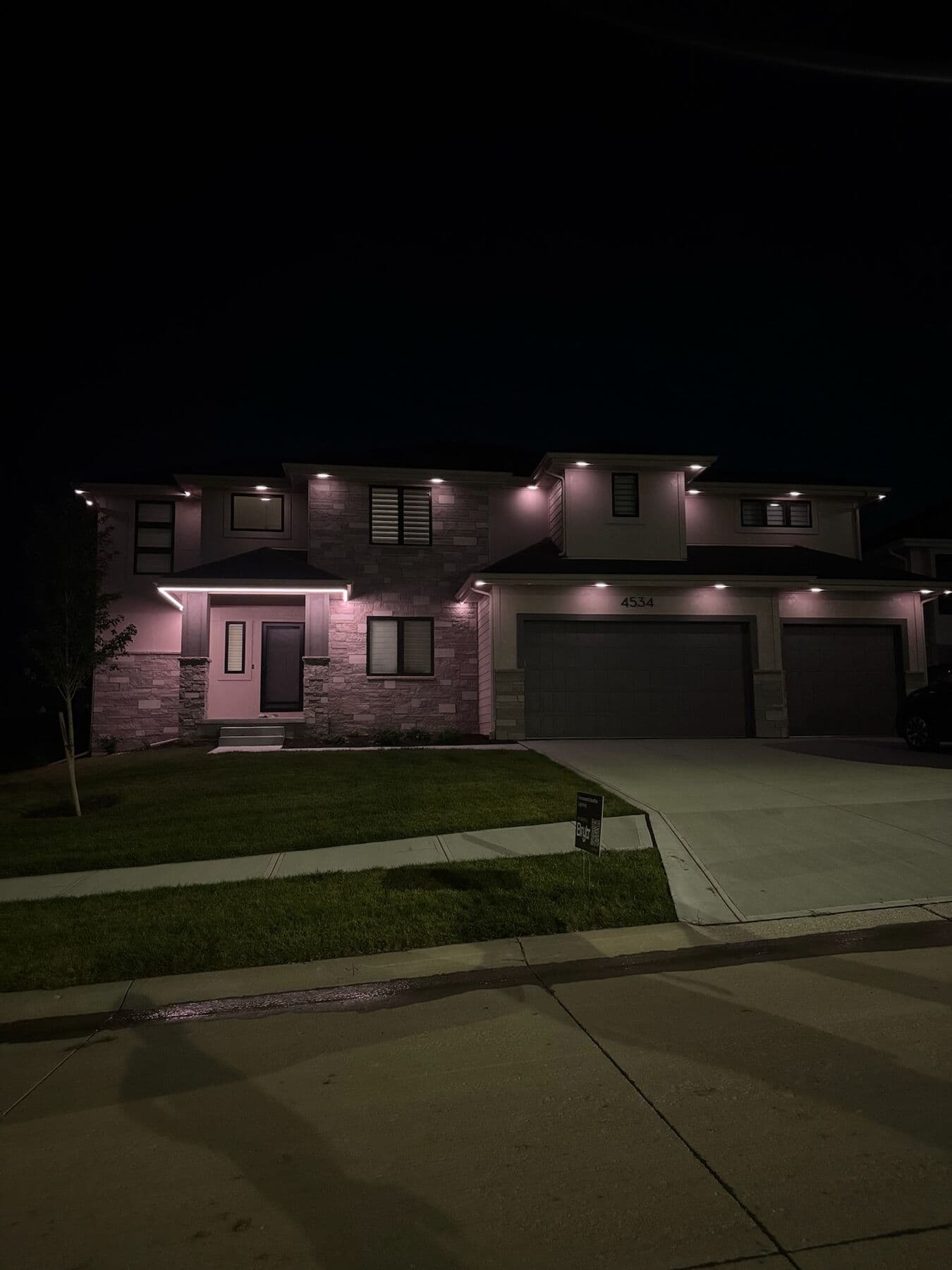 A stone and siding Omaha two-story with evenly spaced warm downlights under the eaves