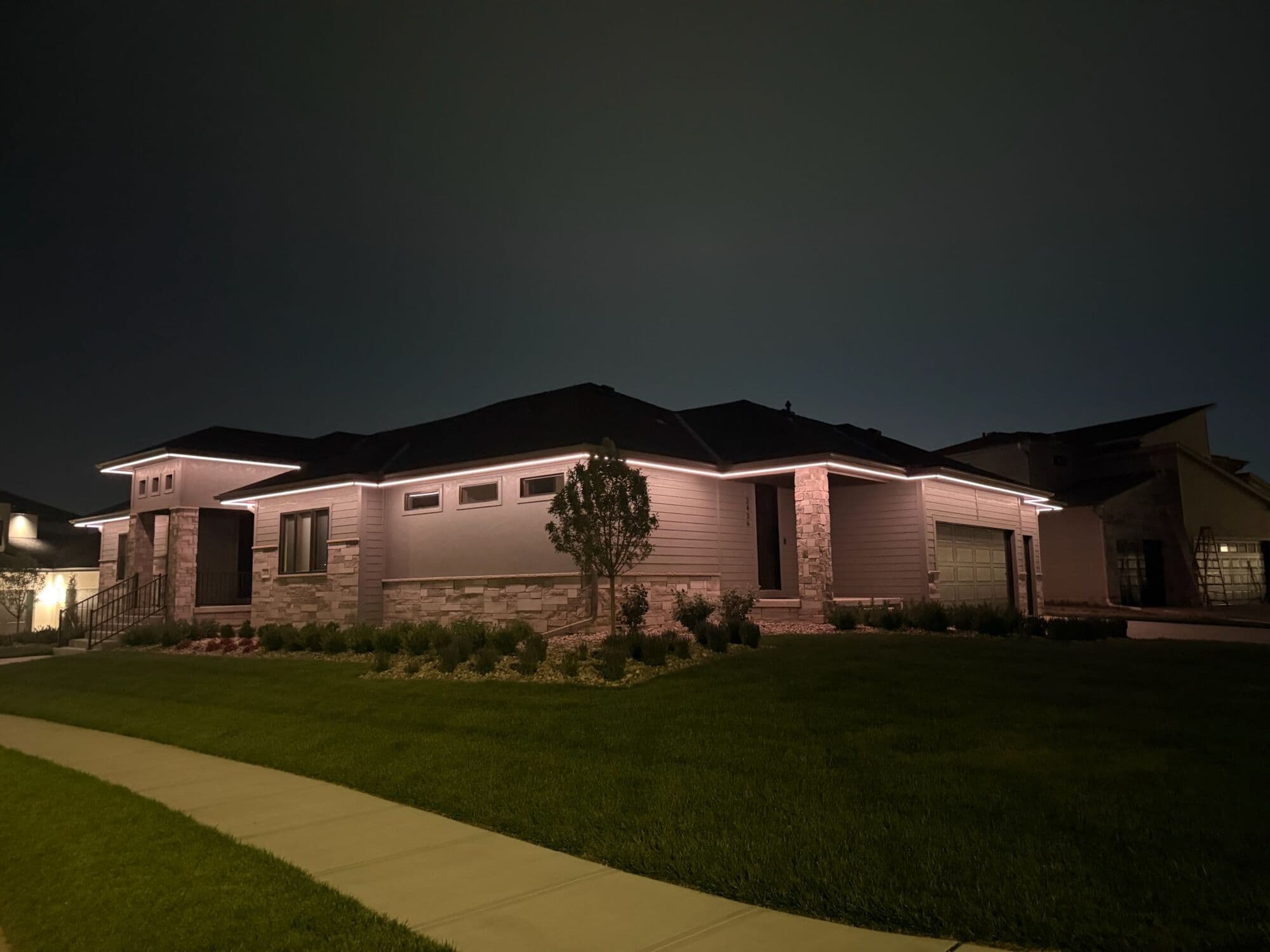 A wide low Omaha ranch at night with warm white holding a straight line the full length of the roof