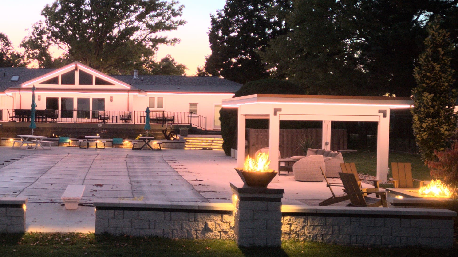 Lit pergola, pool deck and fire bowls at an Omaha home at dusk