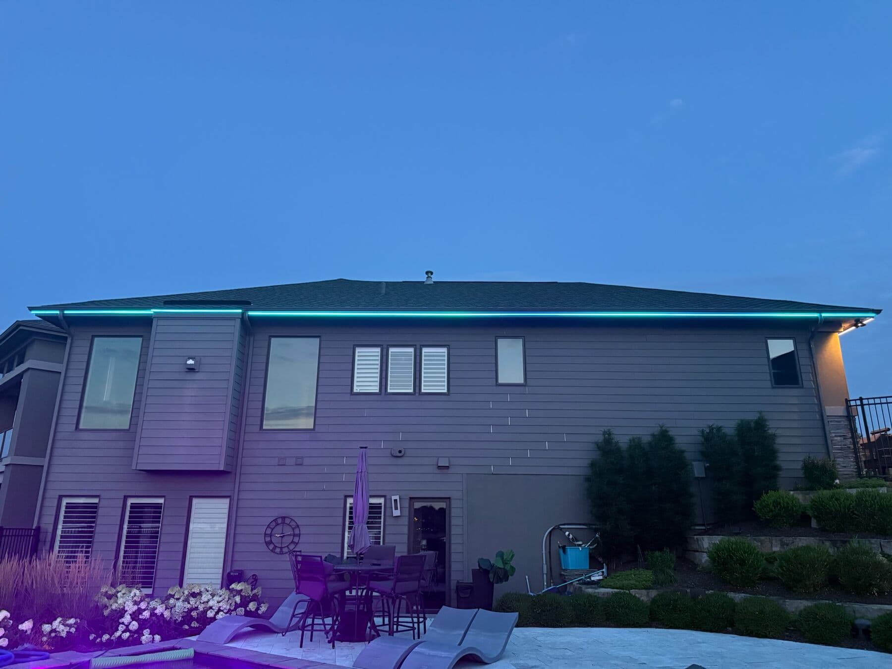 The back of an Omaha home at dusk with the roofline in teal and the patio furniture below washed violet