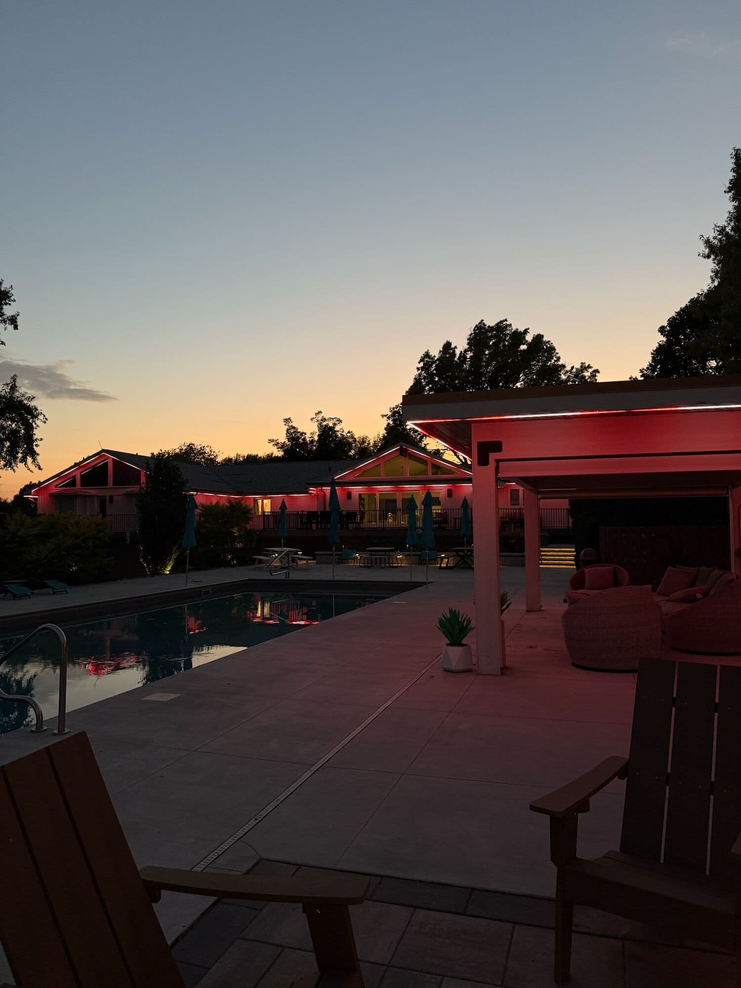 A pool and covered pergola at an Omaha home at sunset, the pergola beam and the far roofline both lit warm