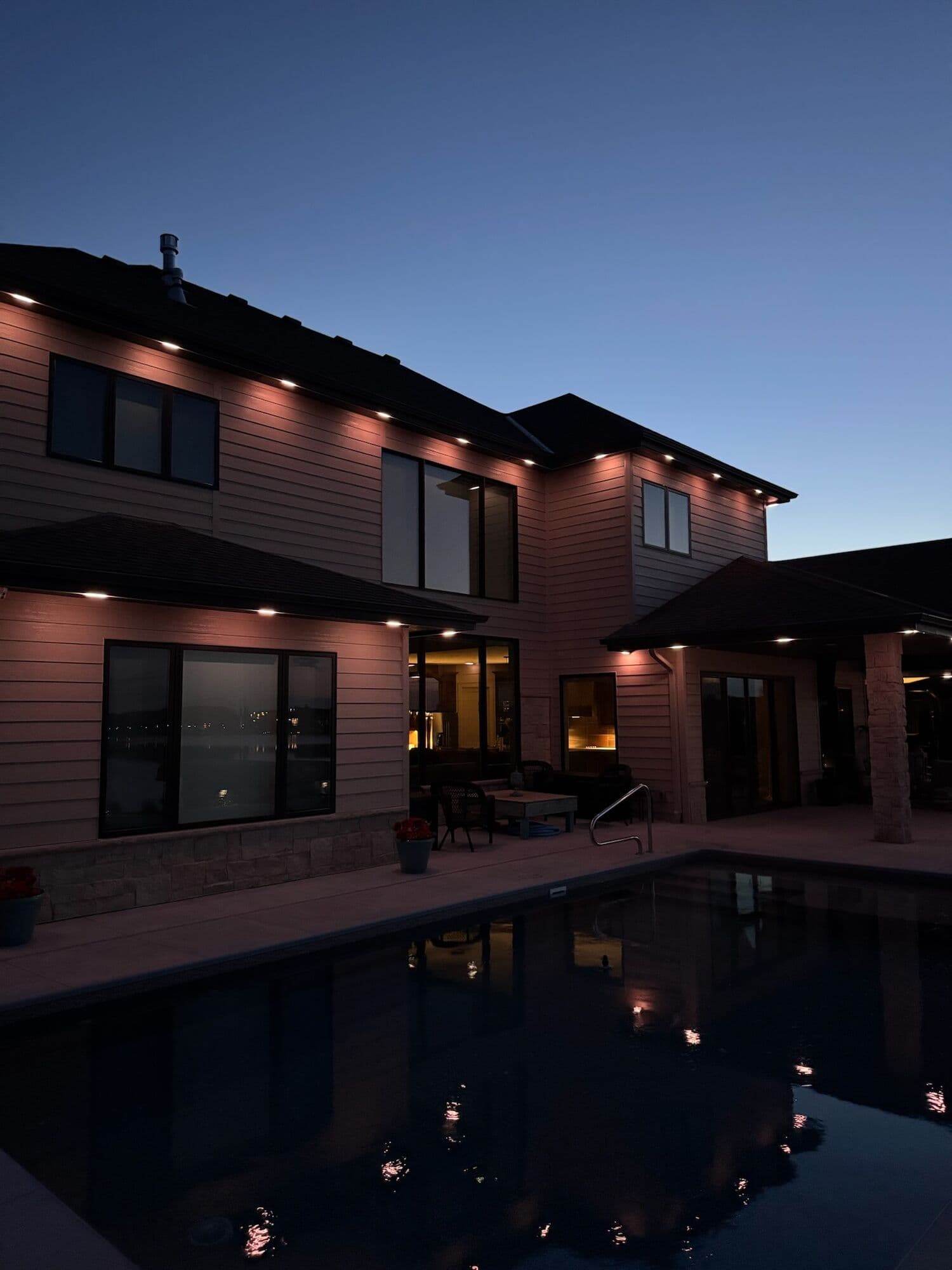 The back of an Omaha home at dusk with warm soffit downlights above a pool, the points repeated in the water