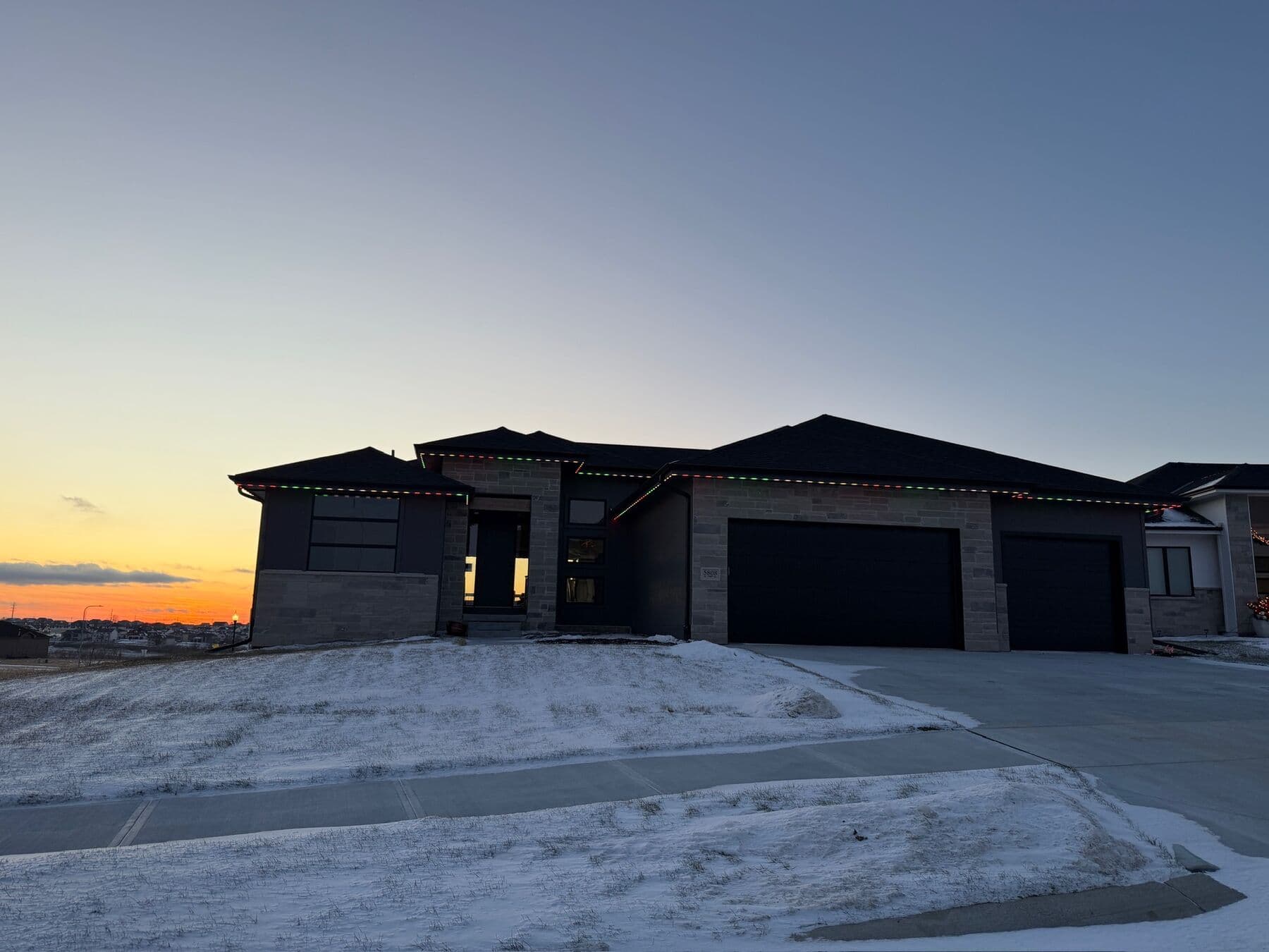 A modern Omaha home at dusk above a snow-covered driveway with a warm run along the roofline